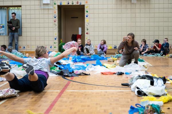 Two people dance amidst plastic debris, inside a circle of watching children.