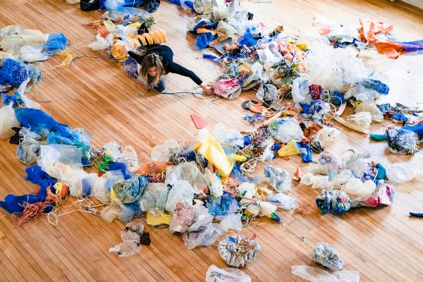 A woman dances on the floor in a room full of plastic debris