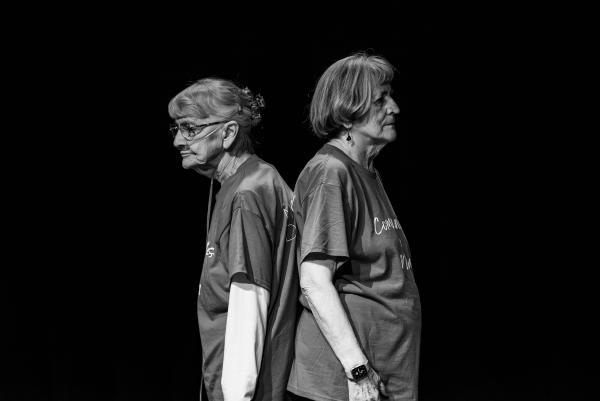 Elderly dancer in blue shirt against black background, arms reaching