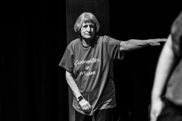 Elderly dancer in blue shirt against black background, arms reaching