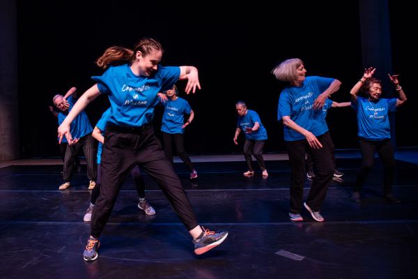 Group of elderly dancers in blue shirts against black background in free flow dance party energy