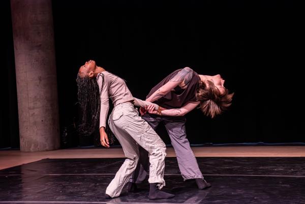 One black and one white dancer are holding hands and are in a back arch