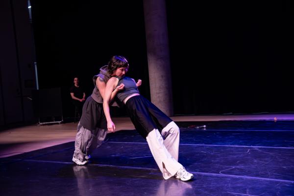 Two white dancers lean against each other creating a triangle