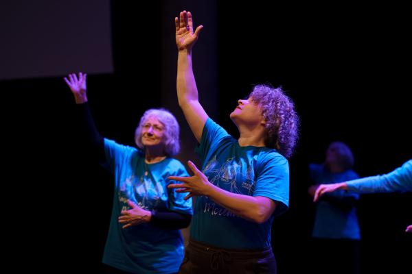 women in blue shirts raise one arm over head