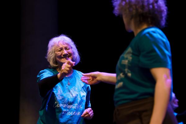 Two women reach toward each other wearing blue shirts.