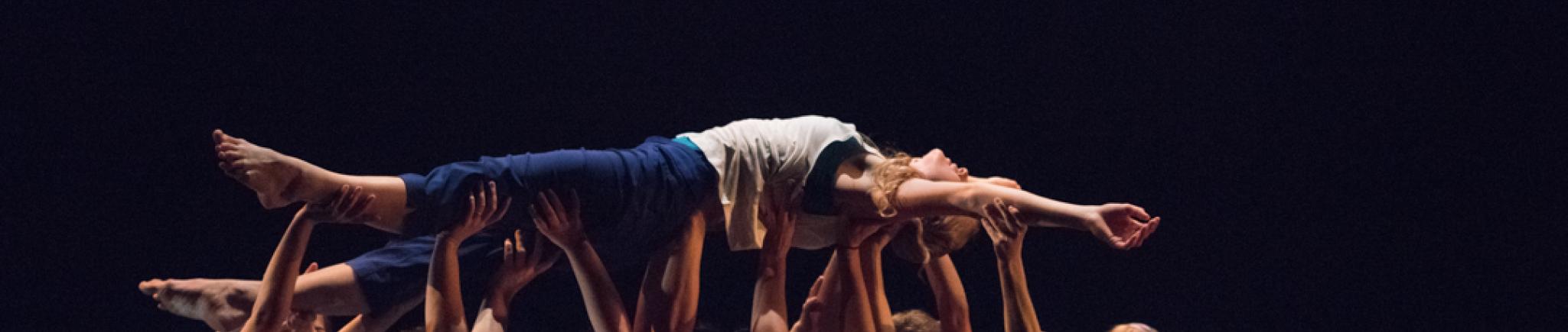 A photo of a dancer being held up high and horizontal, by many other dancers.