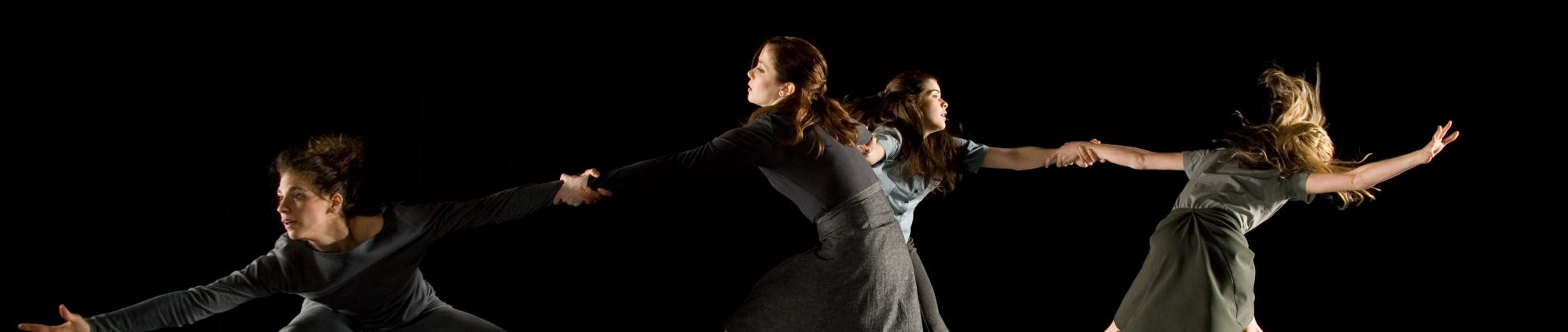 Four dancers hold each other's arms in a line. 