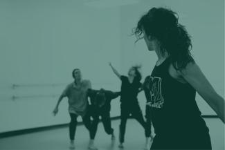 A woman looks back towards three people dancing in a bright studio.