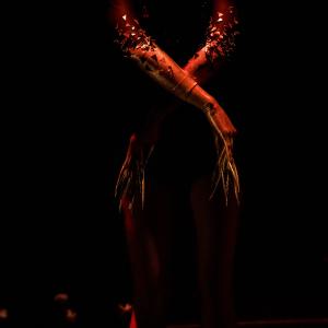 A dancer crosses their forearms in front of their waist, letting their golden gloved hands hang down.