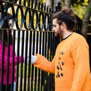 A man in orange shakes hands with a woman in pink through an iron fence.