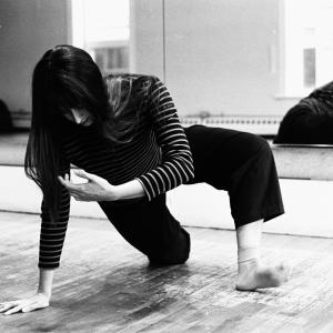 A dancer in black pants and a striped shirt step plants one foot and one hand from a kneeling position