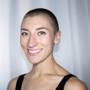 A white woman with buzzed hair smiles widely.