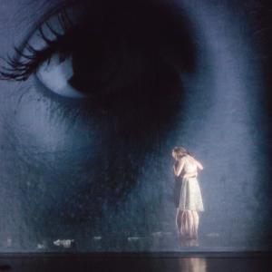 Two dancers hug on stage in front of a photo projection. 