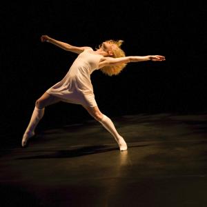 A dancer in a white dress reaches back. 