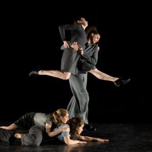 Two dancers lay on the floor below two dancers in a partnering lift.