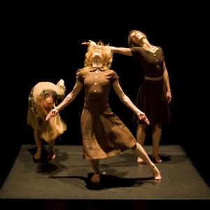 Three dancers in brown dresses are in motion. 