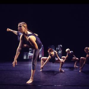 A dancer stands with a leg extended in font of three other dancers.