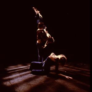 A duet moves behind a dancer sitting on the ground. 