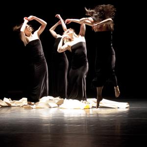 Three dancers stand on piece of canvas, while another jumps in front of them.