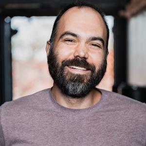 A man with short dark hair and a short beard smiles at the camera.