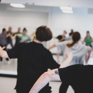 A group of people dance in a studio in front of a mirror.