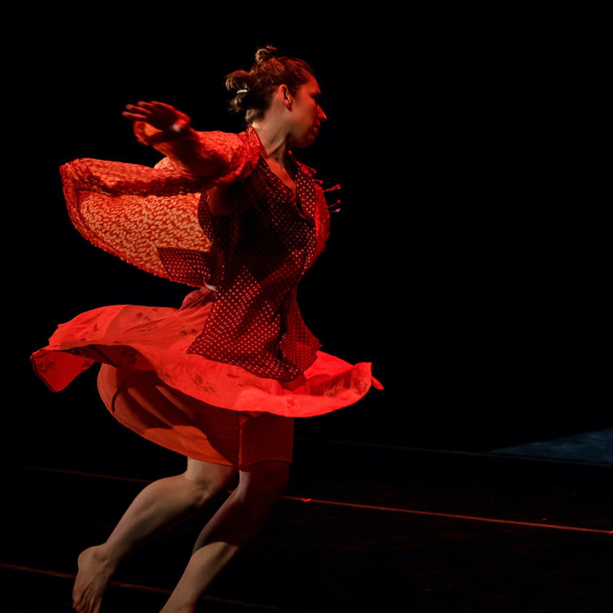 A women in a red dress spins with outward momentum falling forward. 