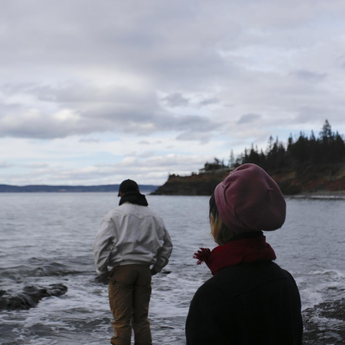 Two people look out on a grey ocean.