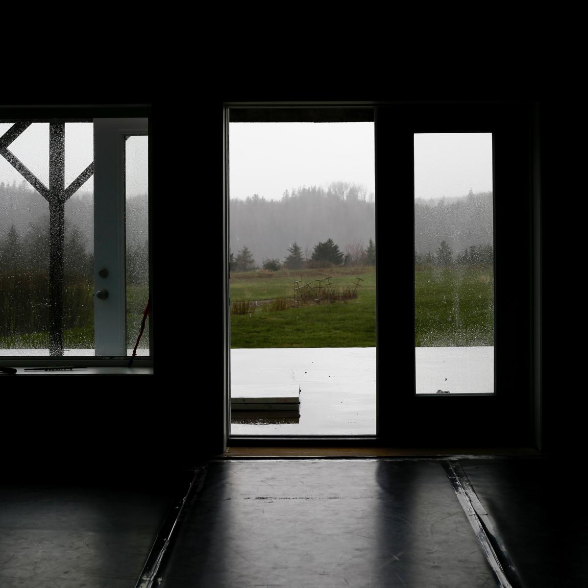  A dark room with an open door and windows showing a rainy landscape