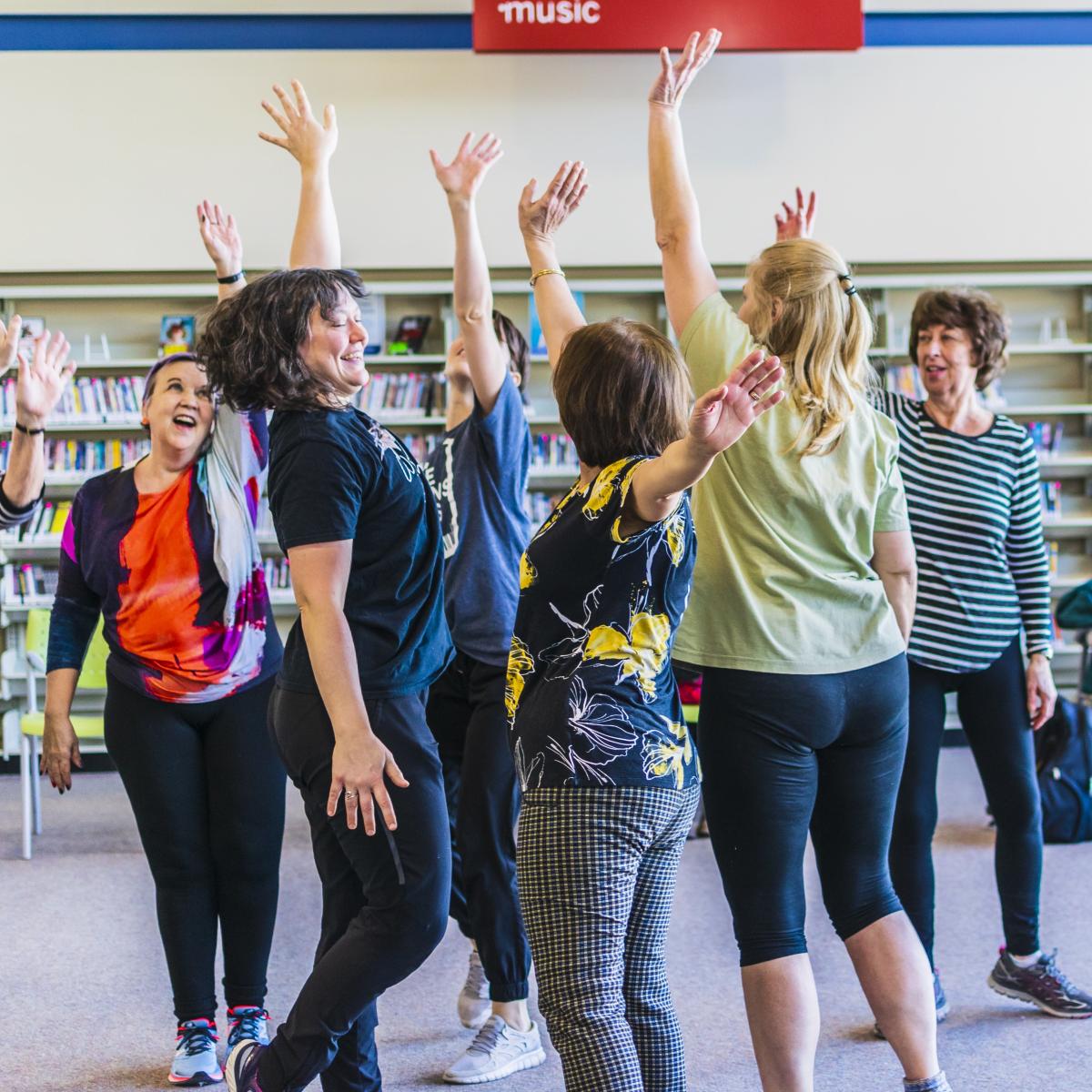 A group of smiling people dance in a library.
