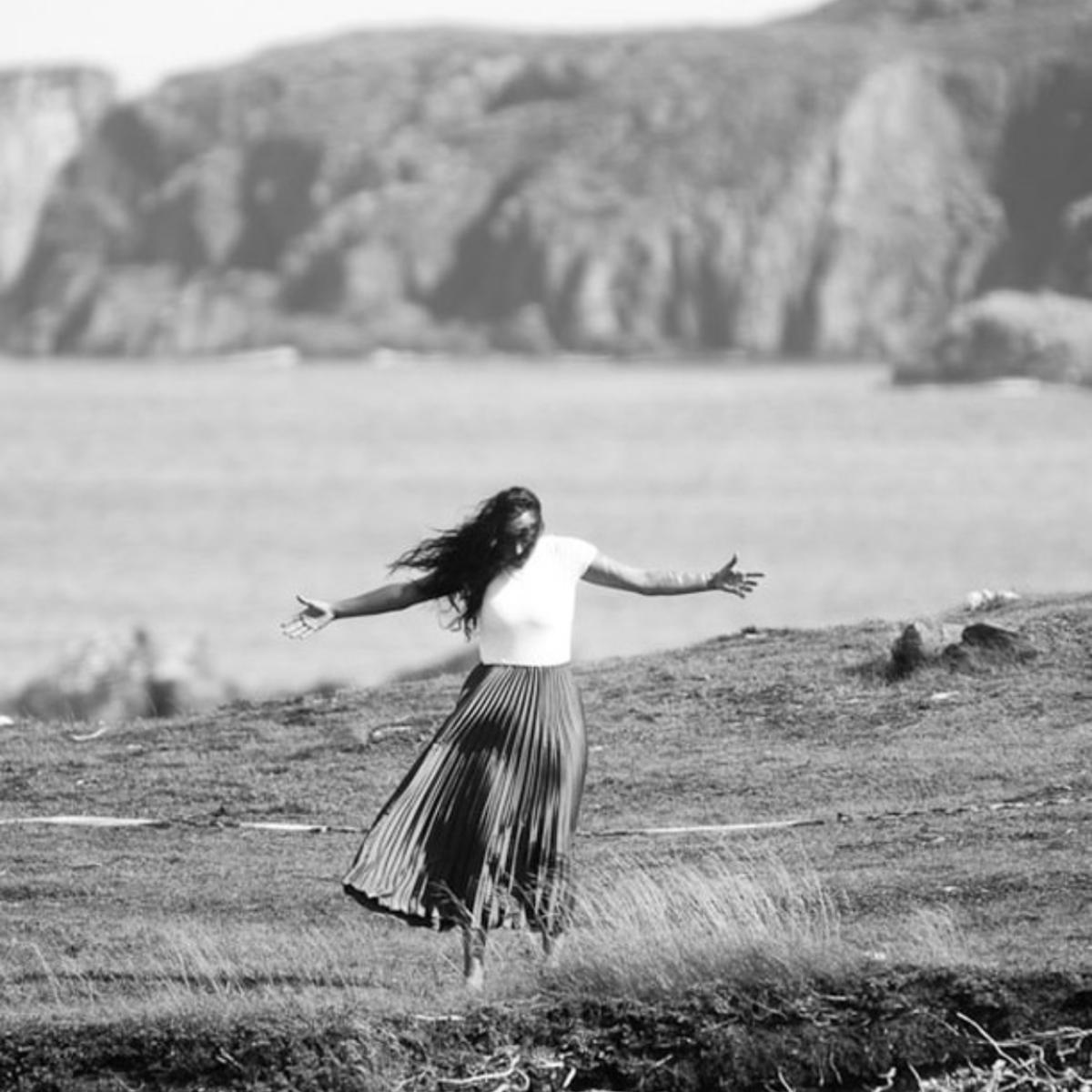 A woman dances on a cliff by the ocean.