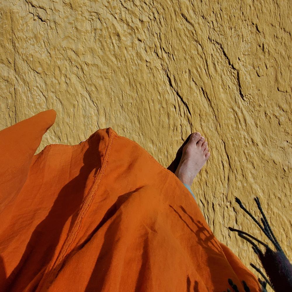 A foot on a beige rocky surface, peeking out from an orange skirt.