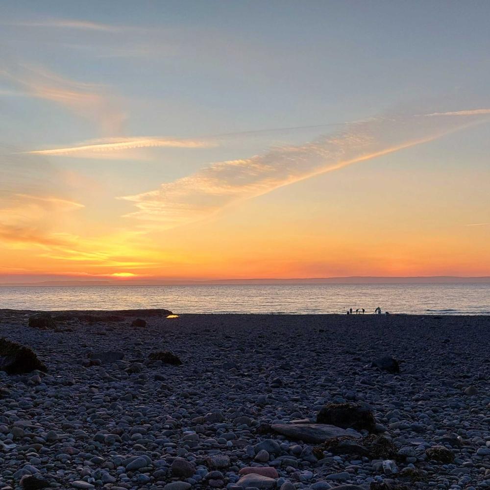 Sunset at a rocky beach with distant figures silhouetted at the waters edge.