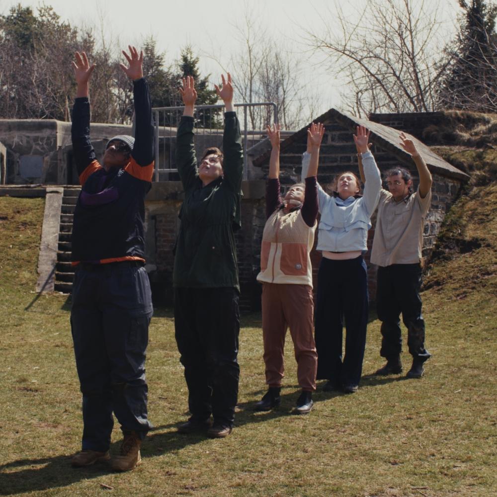 Five dancers in a line with their hands raised